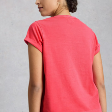 Load image into Gallery viewer, A woman shown from the back wearing a short-sleeve crewneck t-shirt in a vibrant coral pink color, set against a neutral gray textured background.

