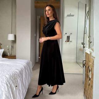 Woman in a black dress standing in a modern bedroom and bathroom.