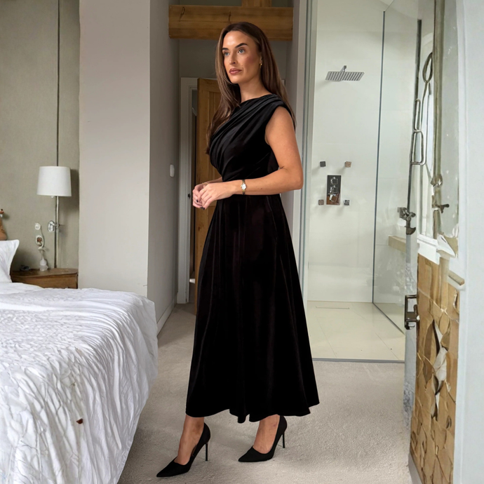 Woman in a black dress standing in a modern bedroom and bathroom.