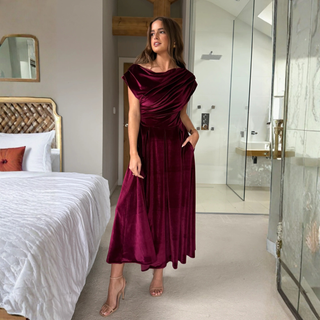 Woman in a burgundy dress standing in a modern bedroom.