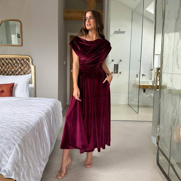 Woman in a burgundy dress standing in a modern bedroom.