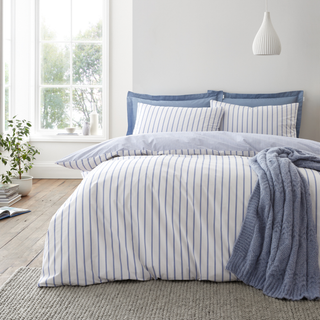 Bed with striped bedding and blue pillows in a bright bedroom.