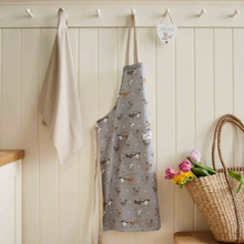 Load image into Gallery viewer, Gray apron with dog pattern hanging on a wall next to a basket of flowers and a towel.
