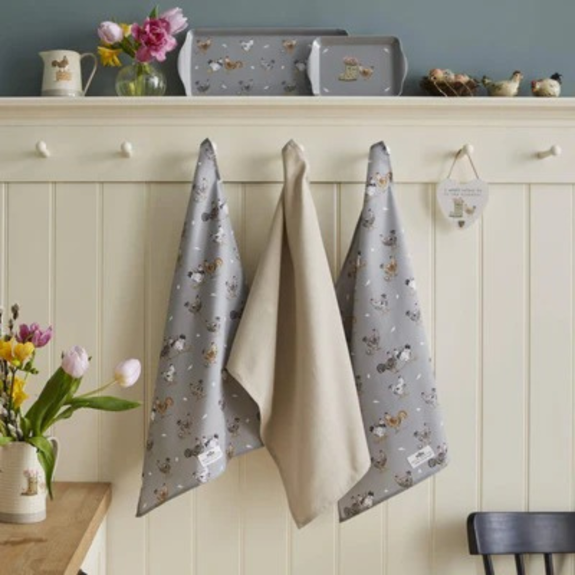 Three kitchen towels hanging on a rack with decorative items in the background.