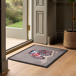 Decorative doormat with a tractor design on a wooden floor in front of a door.