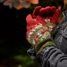 Load image into Gallery viewer, A close-up of a person wearing a pair of hand-knit winter gloves. The gloves feature a red base with a multicolor Fair Isle pattern in white, green, orange, and yellow, and a solid olive green cuff.
