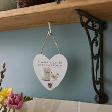 Load image into Gallery viewer, Heart-shaped hanging sign with garden-themed design and text, placed on a shelf with flowers and a decorative bracket.
