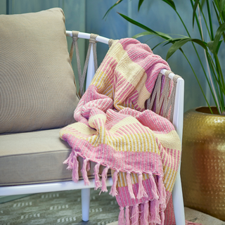 Pink and yellow patterned blanket draped over a white chair with a plant in the background.