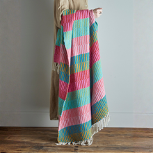Load image into Gallery viewer, Colorful striped blanket draped over a person on a wooden floor with a neutral background
