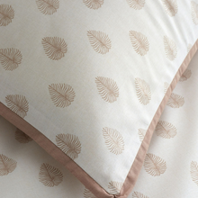 Load image into Gallery viewer, A close-up of a pillow or cushion cover with a repeating leaf motif in a warm taupe-brown on an off-white fabric, finished with a matching taupe-brown piped edge.
