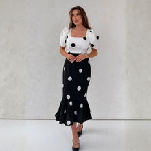 Load image into Gallery viewer, Woman wearing a white top with black polka dots and a black skirt with white polka dots against a plain background.
