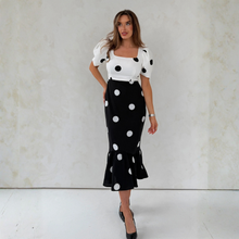 Load image into Gallery viewer, Woman wearing a white top with black polka dots and a black skirt with white polka dots against a light background.
