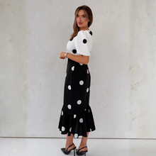 Load image into Gallery viewer, Woman wearing a black and white polka dot dress against a plain background
