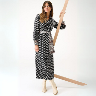 Woman in a black and white patterned dress holding a long wooden stick against a white background
