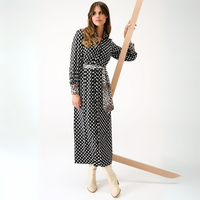 Woman in a black and white patterned dress holding a long wooden stick against a white background