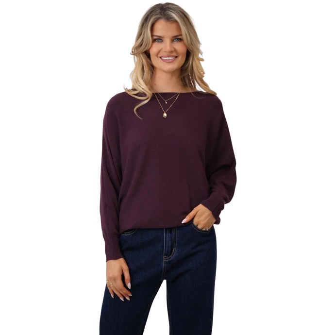 Woman wearing a dark purple sweater and blue jeans on a white background