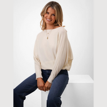 Load image into Gallery viewer, Woman wearing a cream sweater and blue jeans sitting on a white stool against a white background
