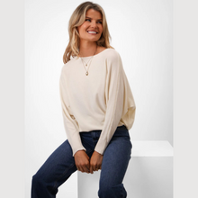 Load image into Gallery viewer, Woman wearing a cream sweater and blue jeans sitting on a white surface with a white background
