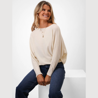 Woman wearing a cream sweater and blue jeans sitting on a white surface with a white background