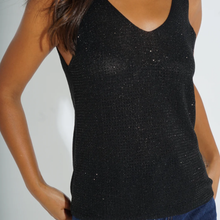 Load image into Gallery viewer, A close-up of a woman wearing a black sleeveless knit top with subtle shimmering sparkles, paired with blue jeans against a plain light background.
