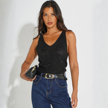 Load image into Gallery viewer, A woman modeling a black sparkly knit V-neck tank top paired with blue jeans and a black belt, holding a small black handbag against a plain light background.

