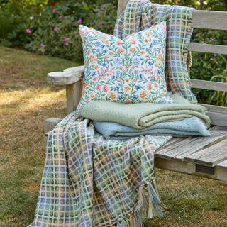 Floral pillow and blankets on a wooden bench outdoors