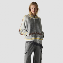 Load image into Gallery viewer, A woman modeling a gray knit zip-up sweater with yellow, brown, and white geometric patterns, paired with gray pinstriped pants, against a light gray studio background.
