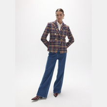 Load image into Gallery viewer, A model stands against a plain white studio background wearing a double-breasted plaid blazer in navy, gold, and beige tones, paired with wide-leg blue jeans and dark brown pointed shoes.
