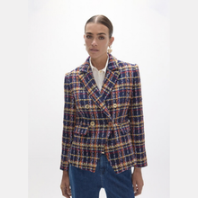 Load image into Gallery viewer, A woman modeling a double-breasted tweed blazer with a navy, red, and gold plaid pattern, worn over a white collared shirt and blue jeans against a plain white studio background.
