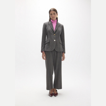 Load image into Gallery viewer, A model stands against a plain white studio background wearing a gray pinstripe blazer and matching wide-leg trousers over a bright pink turtleneck, with dark red pointed shoes.
