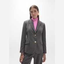 Load image into Gallery viewer, A woman modeling a dark gray pinstripe blazer with gold buttons, worn over a bright pink turtleneck, against a plain white studio background.
