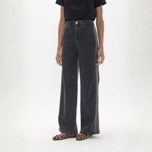 Load image into Gallery viewer, A model wearing a pair of dark gray wide-leg jeans with silver studs down the side, paired with a black t-shirt and leopard print flat shoes, against a plain white studio background.
