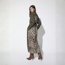 Load image into Gallery viewer, A woman models a long-sleeved maxi dress with an olive green collar, cuffs, and back, paired with a beige and brown leopard print front and skirt. She is wearing brown pointed-toe heeled boots against a plain white studio background.
