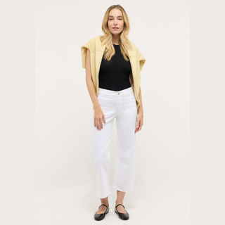 Woman wearing a yellow vest, black top, white pants, and black shoes on a white background