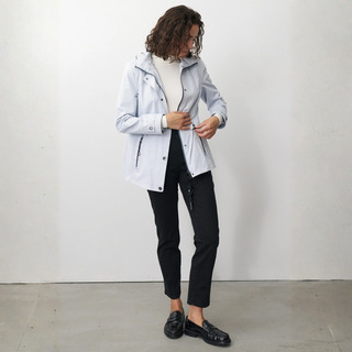 Person wearing a light gray jacket over a white shirt, black pants, and black shoes on a plain background