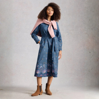 Woman wearing a blue floral dress with a pink scarf against a gray background