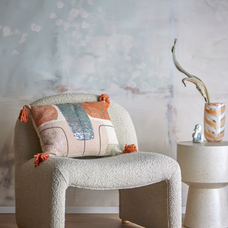 Decorative pillow on a textured chair with a side table and vase in the background