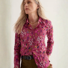 Load image into Gallery viewer, A woman wearing a long-sleeve button-up shirt in a dusty pink crinkle fabric with a colorful floral print, paired with brown pants and a black belt.
