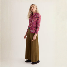 Load image into Gallery viewer, A woman stands in a studio wearing a pink floral long-sleeve button-up shirt with a black belt and wide-leg olive brown trousers.
