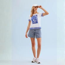 Load image into Gallery viewer, Woman in White T with Blue Palm tree print and shorts on pale background 
