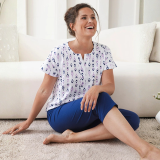 Woman sitting on the floor in a living room, wearing a patterned top and blue shorts.