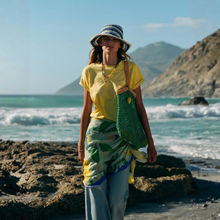 Load image into Gallery viewer, Person standing on a rocky beach with ocean and mountains in the background

