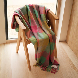 Colorful plaid blanket draped over a wooden chair in a room with light wood flooring and a window.