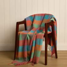Load image into Gallery viewer, A multicolor plaid wool throw blanket draped over a dark wooden armchair in a room with cream paneled walls and light wood flooring.
