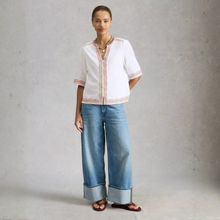 Load image into Gallery viewer, Woman wearing a white embroidered top and blue jeans against a gray background
