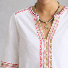 Load image into Gallery viewer, White blouse with colorful embroidery and a necklace on a plain background
