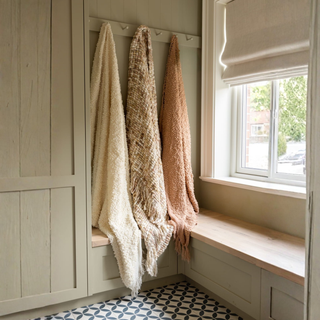 Wooden bench with three hanging blankets in a room with a window and patterned floor.