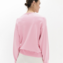 Load image into Gallery viewer, A woman shown from the back wearing a light pink cropped long-sleeve sweatshirt and white pants against a plain white studio background.
