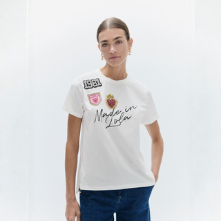 A woman modeling a white short-sleeve t-shirt with 'Made in Lofa' and brand patches on the front, paired with dark blue jeans against a clean white studio background.