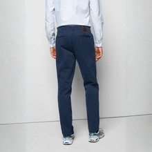 Load image into Gallery viewer, A man viewed from behind wearing navy blue chino pants, a light blue and white striped long-sleeve shirt, and athletic sneakers, standing against a light gray studio background.

